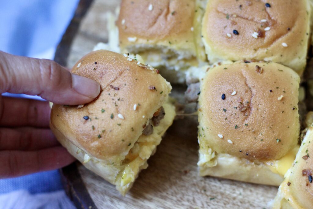 Hawaiian roll breakfast slider being pulled from a tray of sausage, egg and cheese sliders