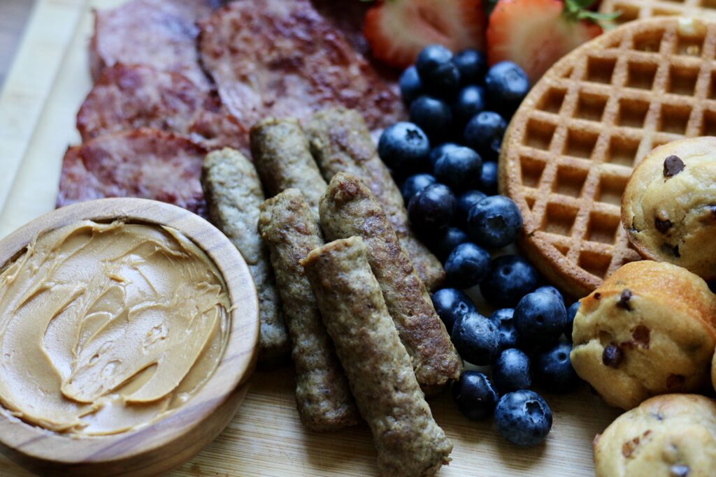 Turkey bacon, chicken sausage, peanut butter, blueberries, waffles, and mini protein muffins on a breakfast board