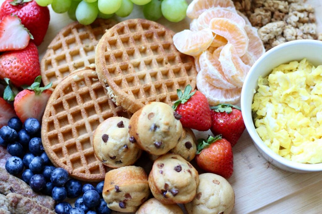 Waffles, mini protein muffins, scrambled eggs, strawberries, blueberries, and mandarin oranges on a breakfast board