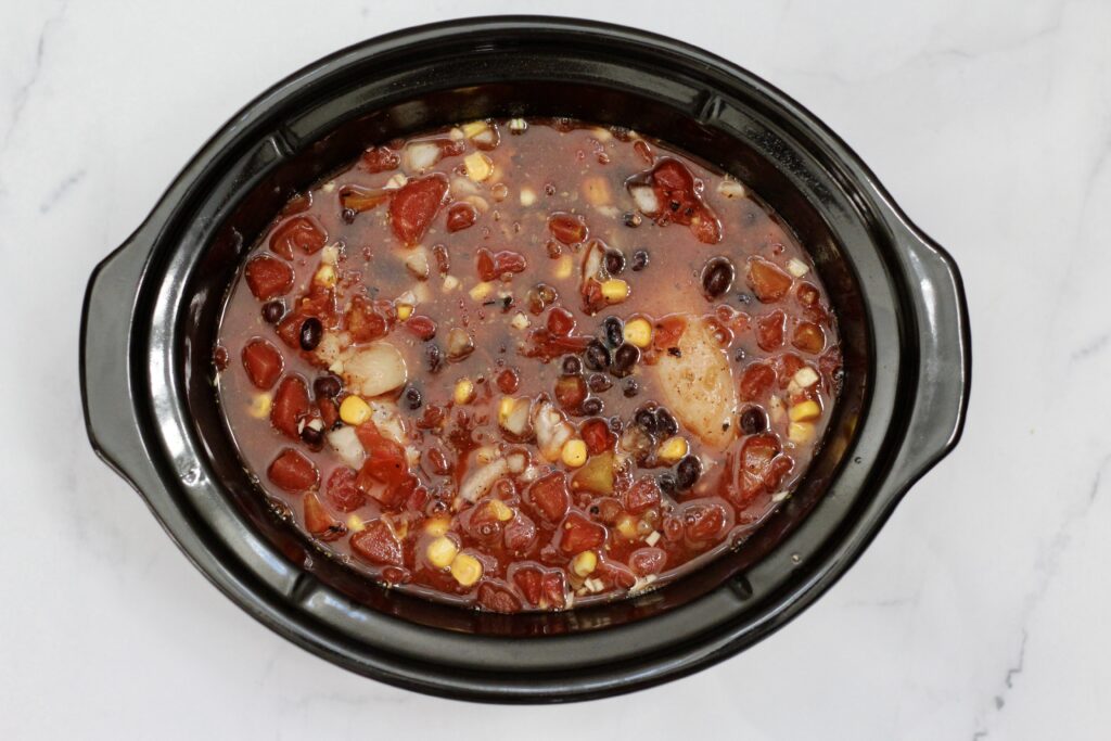Chicken tortilla soup cooking in a slow cooker with tomatoes, black beans and corn.