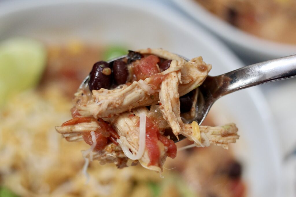 Spoonful of creamy chicken tortilla soup with shredded chicken, black beans and tomatoes.