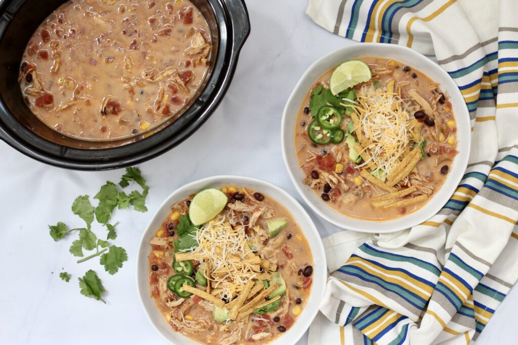 Bowls of creamy slow cooker chicken tortilla soup served beside the Crockpot.