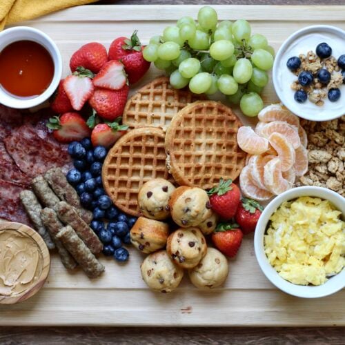High-protein breakfast charcuterie board with waffles, eggs, turkey bacon, sausage, mini muffins, yogurt, and fresh fruit