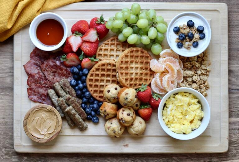 High-protein breakfast charcuterie board with waffles, eggs, turkey bacon, sausage, mini muffins, yogurt, and fresh fruit