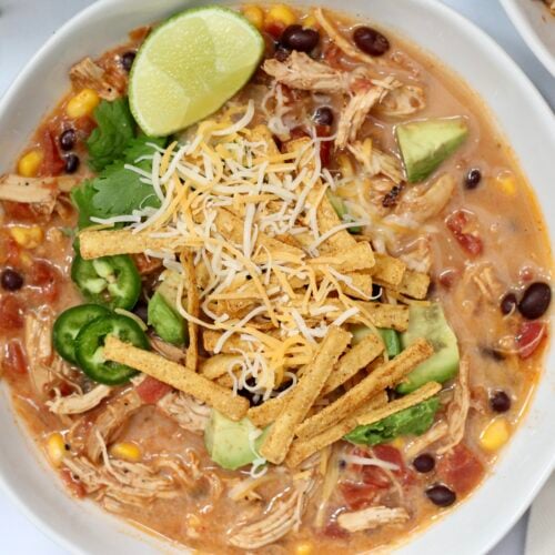 Slow cooker chicken tortilla soup topped with cheese, avocado, jalapeños, cilantro and tortilla strips.