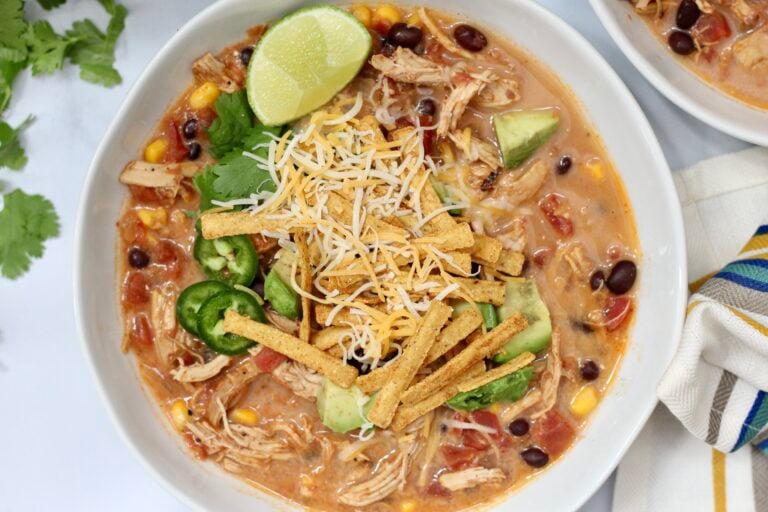 Slow cooker chicken tortilla soup topped with cheese, avocado, jalapeños, cilantro and tortilla strips.