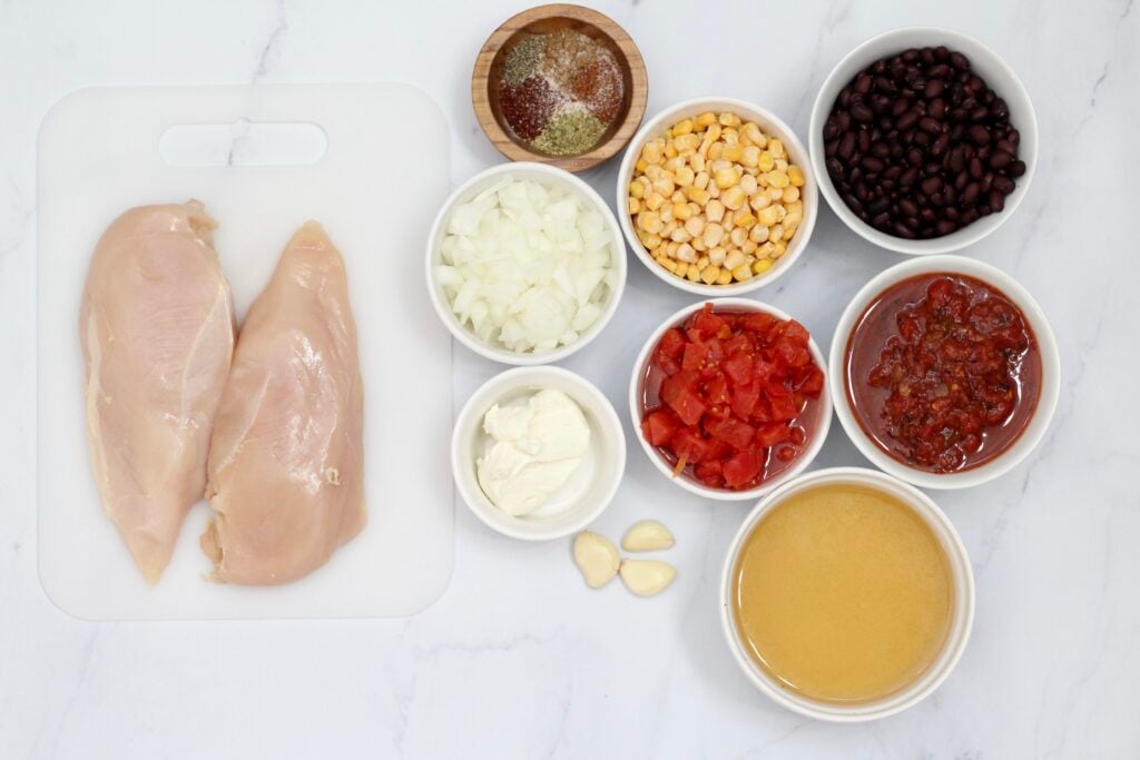 Ingredients for slow cooker chicken tortilla soup arranged on a white surface.